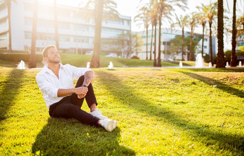 Work life balance concept. Happy young european businessman sitting on grass in park, having break